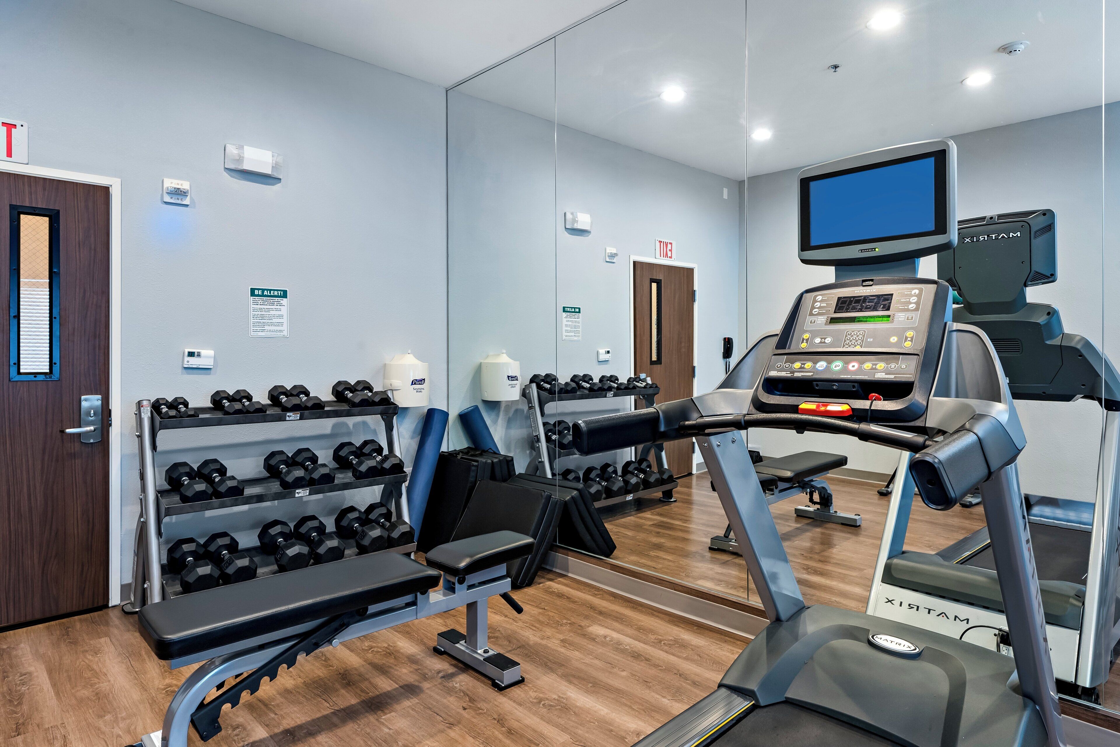 Une salle de sport équipée de tapis de course, d’haltères et d’un mur recouvert de miroirs.