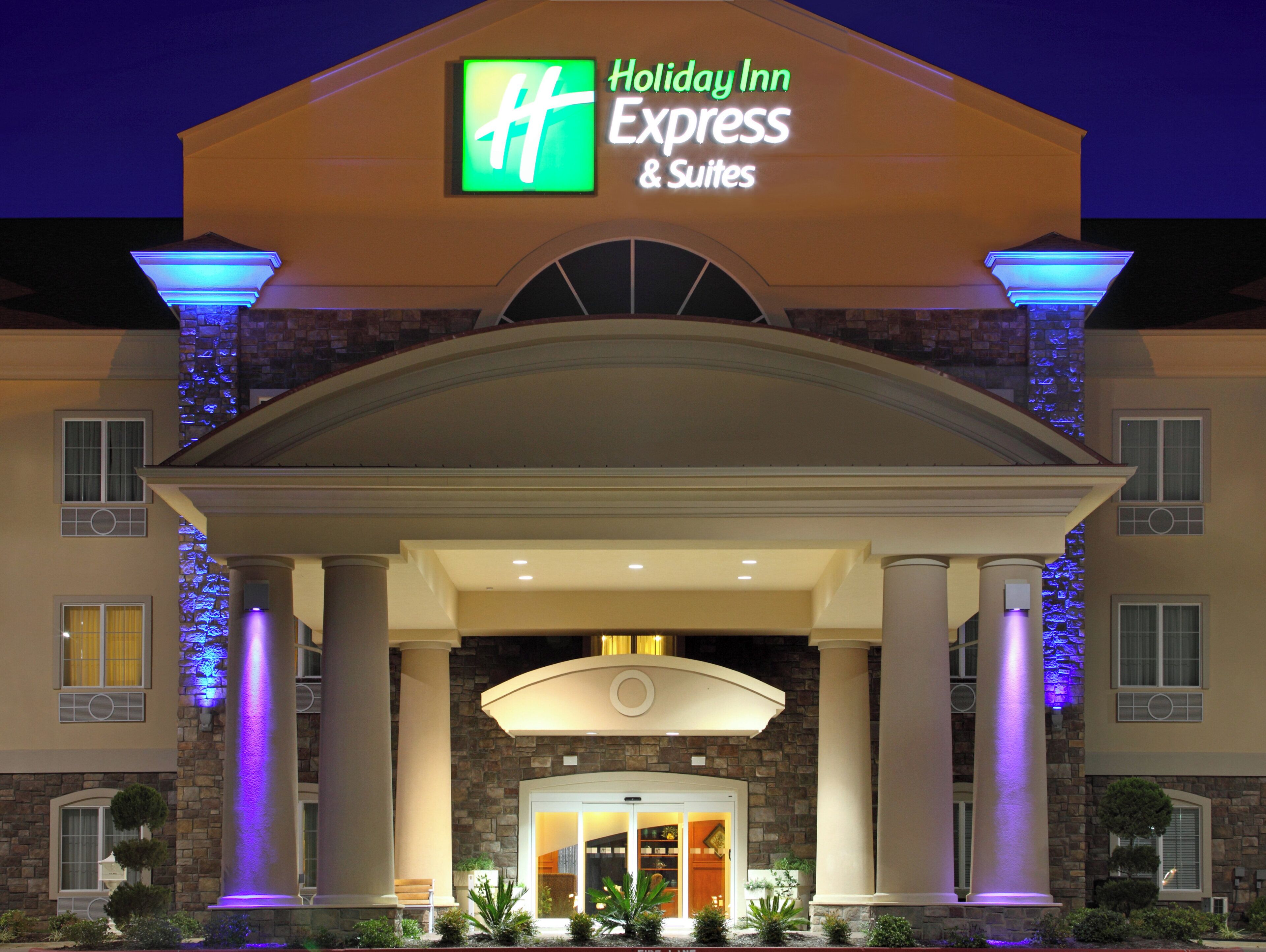 A Holiday Inn Express & Suites building with a prominent entrance, columns, and a stone facade.