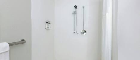 Un bagno bianco con doccia, porta in vetro, soffione a mano, rubinetto a parete e porta asciugamani.