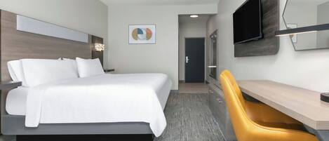 A modern hotel room with a bed, desk, and chair, a flat-screen TV, and a door leading to another room.
