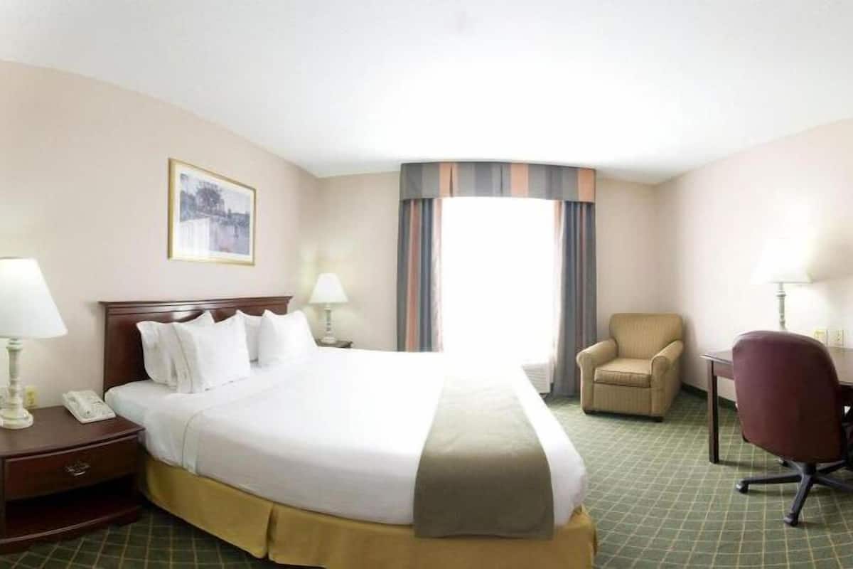 A hotel room with a large bed, two bedside tables with lamps, a chair, a desk, and a window with curtains.