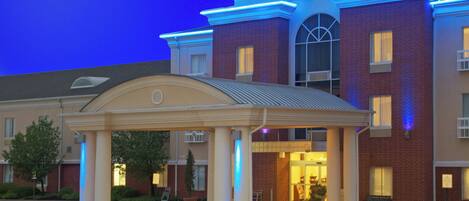 A Holiday Inn Express & Suites building with a covered entrance, brick facade, and illuminated signage.