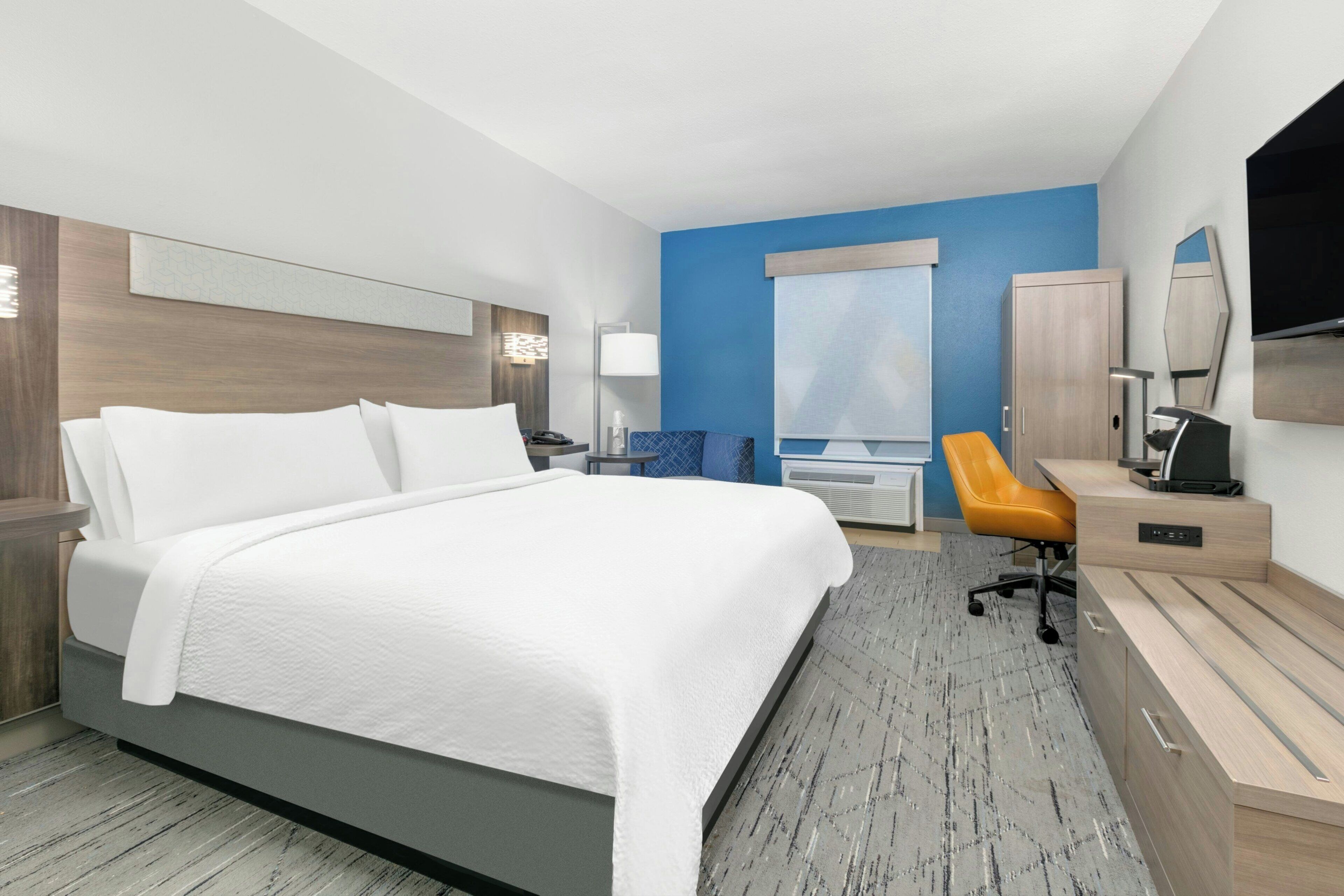 A hotel room with a large bed, a desk with a chair, a television, and a wardrobe.