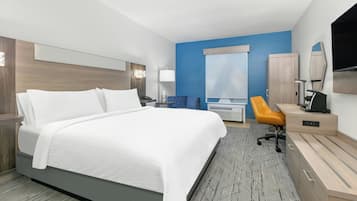 A hotel room with a large bed, a desk with a chair, a television, and a wardrobe.
