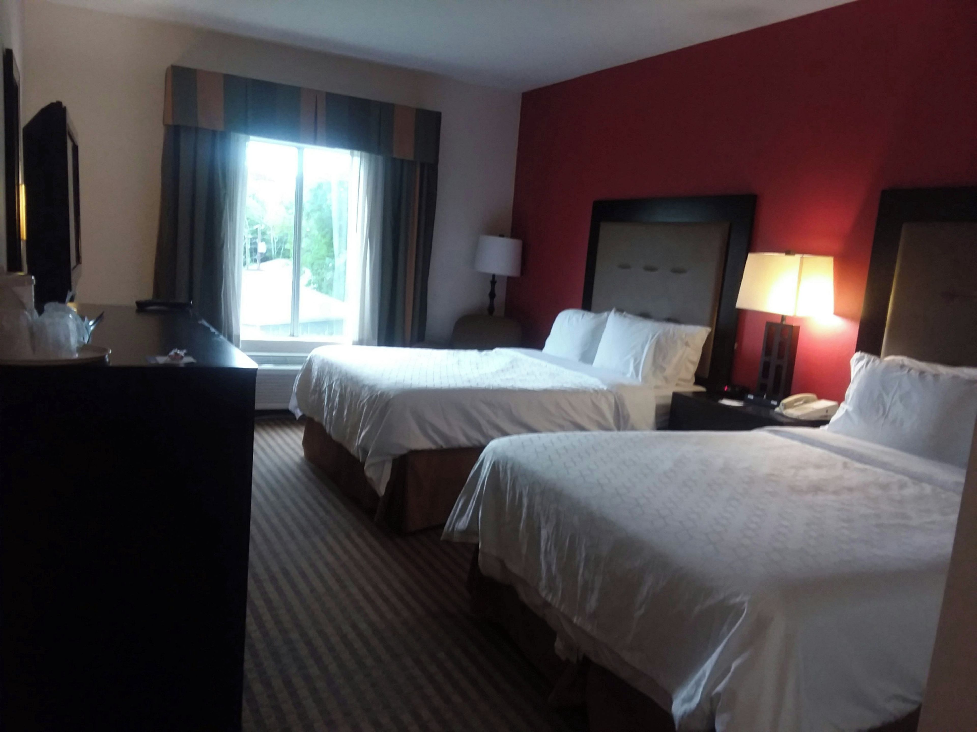 A hotel room with two beds, a desk, a lamp, and a window with curtains.