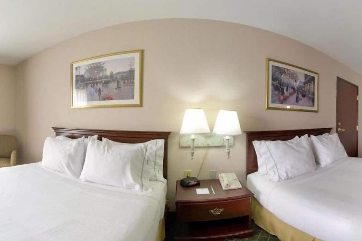 A hotel room with two beds, a chair, a nightstand with a lamp, and two framed pictures on the walls.