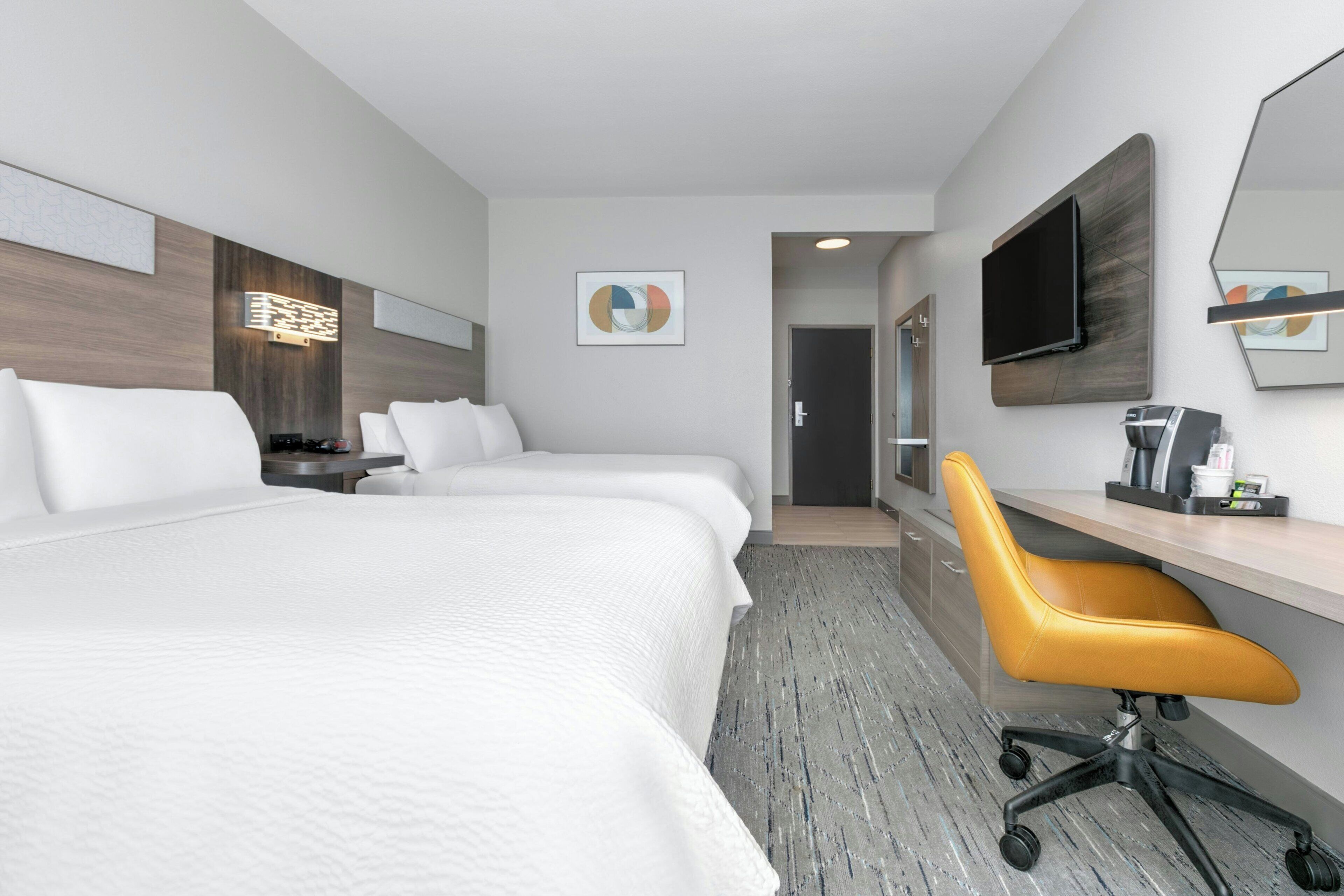 A hotel room with two beds, a desk, a chair, a TV, and a bathroom door.