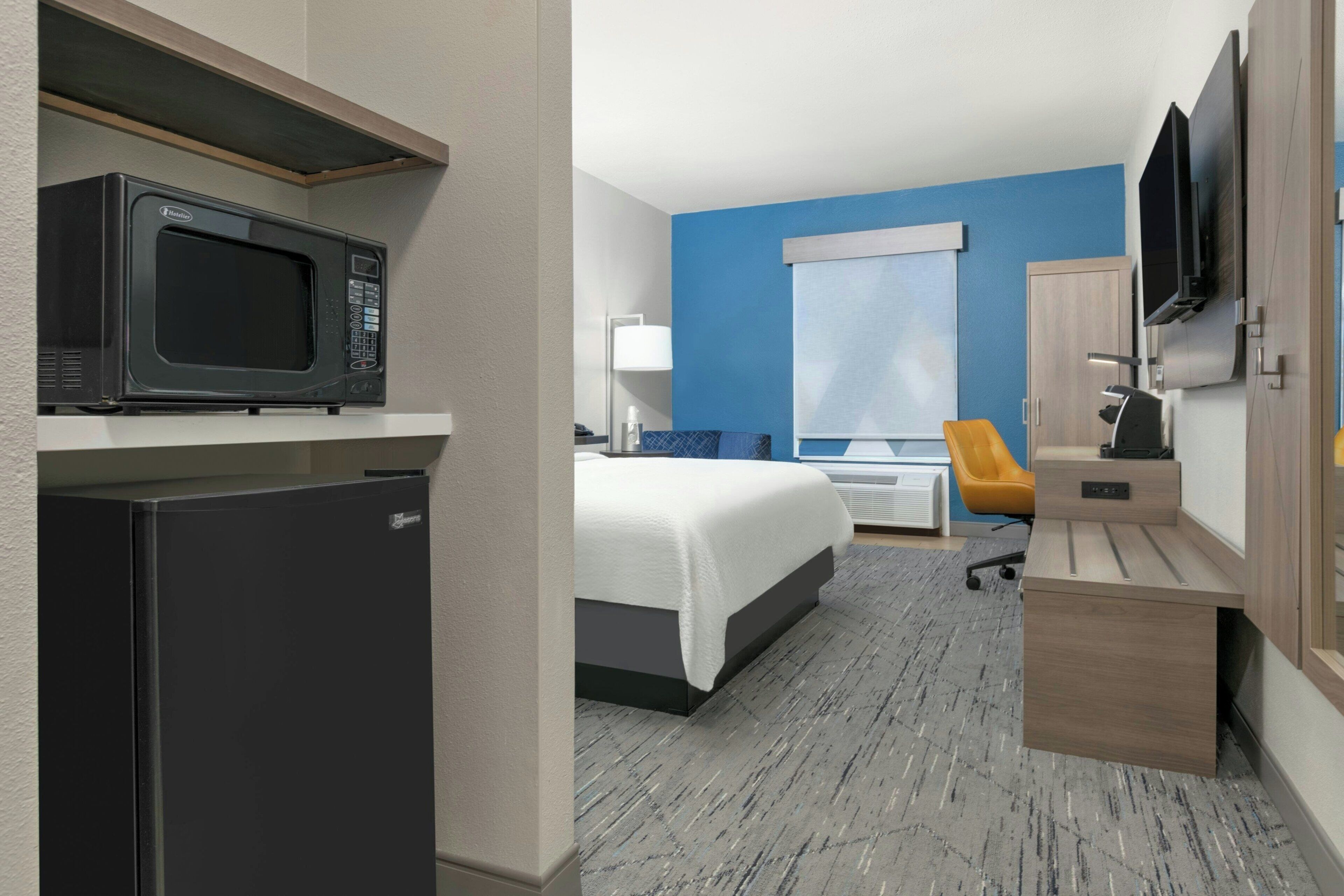A hotel room with a bed, a desk with a chair, a microwave, a television, and a wardrobe.