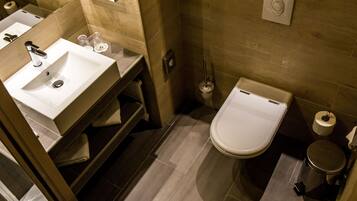 A modern bathroom with a sink, toilet, and a trash bin.