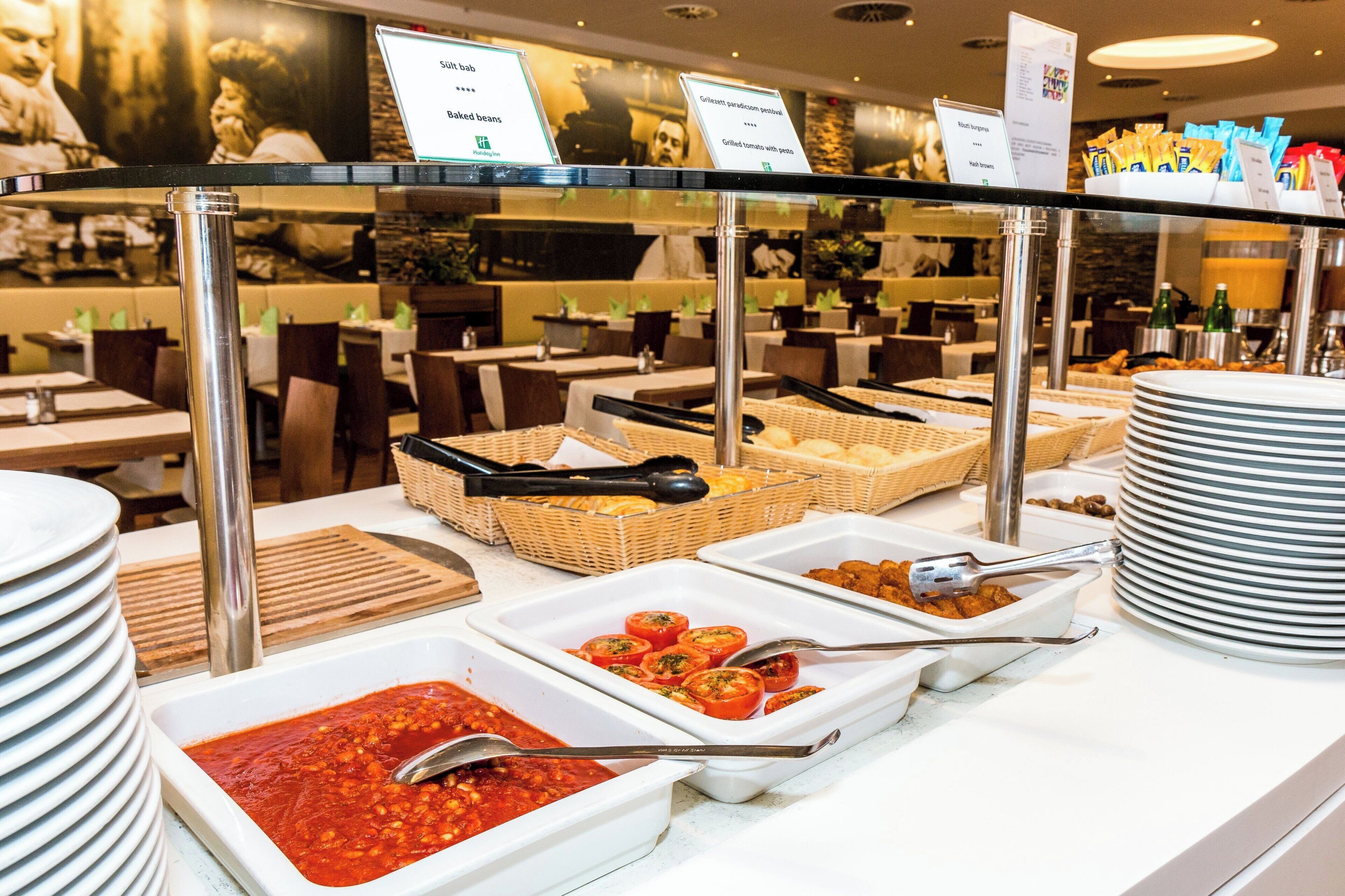 Un buffet proposant une variété de plats, notamment des haricots cuits, des tomates grillées à la sauce pesto et des pommes de terre rissolées.