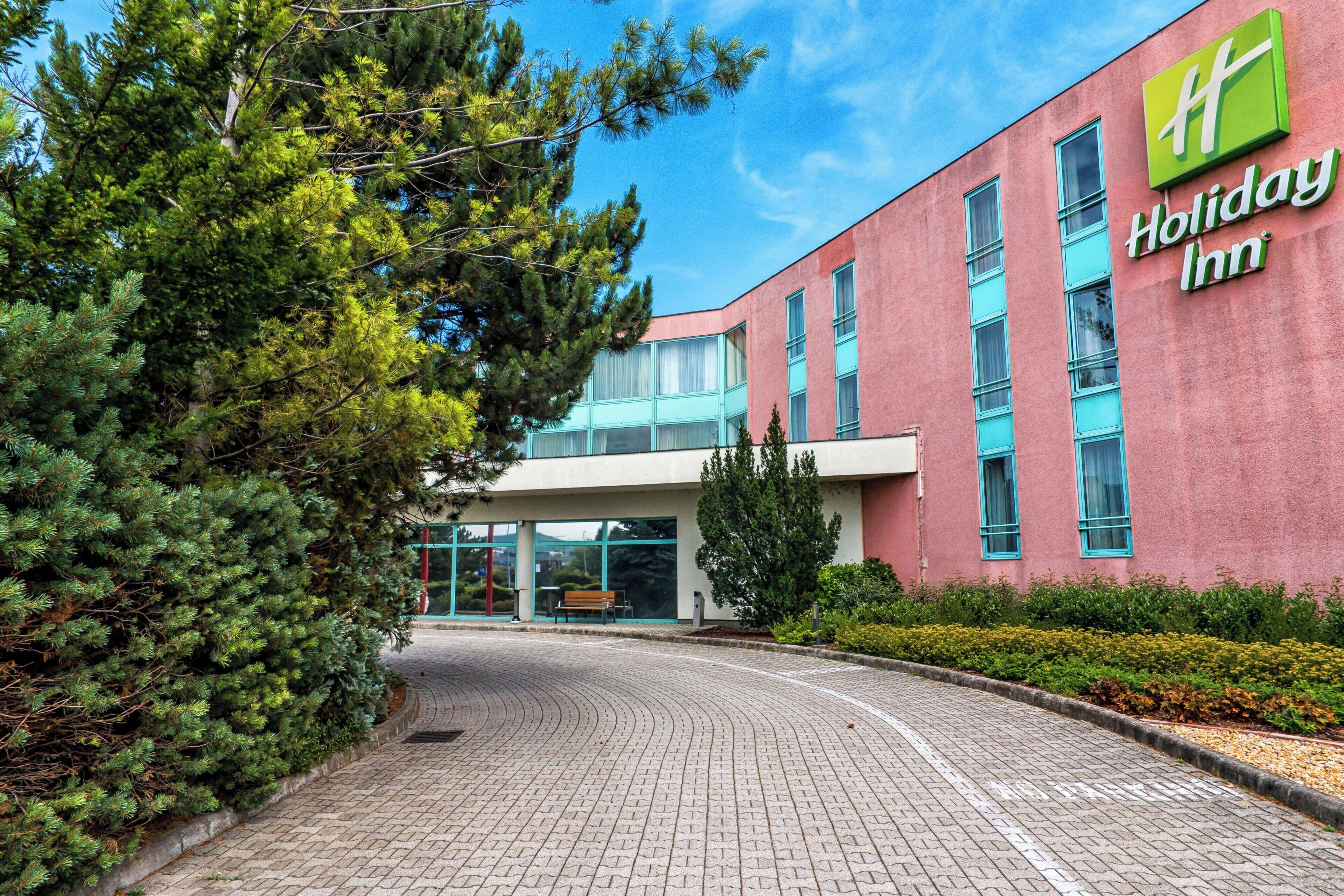 A Holiday Inn hotel with a brick facade, large windows, and a paved entrance area.