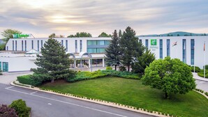 Ein Holiday Inn Hotel mit modernem Design, das eine große Eingangshalle mit überdachten Sitzgelegenheiten, gepflegter Bepflanzung und einem Parkplatz bietet.