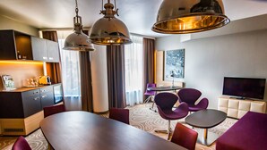 A hotel room with a dining table, purple chairs, a TV, and a large window with curtains. - Holiday Inn Budapest-Budaörs by IHG (Budaors)