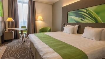 A hotel room with a large bed, a desk, two chairs, a lamp, and a painting on the wall.
