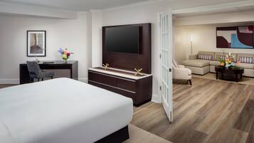 Una habitación de hotel con una cama grande, un escritorio con silla, un televisor montado en la pared, un sofá y una mesa de centro.