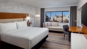Habitación de hotel con una cama grande, un sofá, un escritorio y vistas a un paisaje urbano.