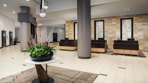 Un moderno vestíbulo de hotel con un mostrador de recepción, pilares grandes y una planta en maceta.