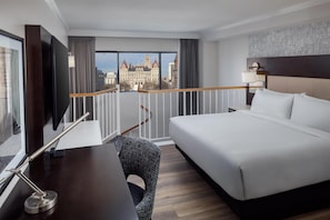 Habitación de hotel con una cama grande, un escritorio con computadora, televisión y balcón con vista a la ciudad.