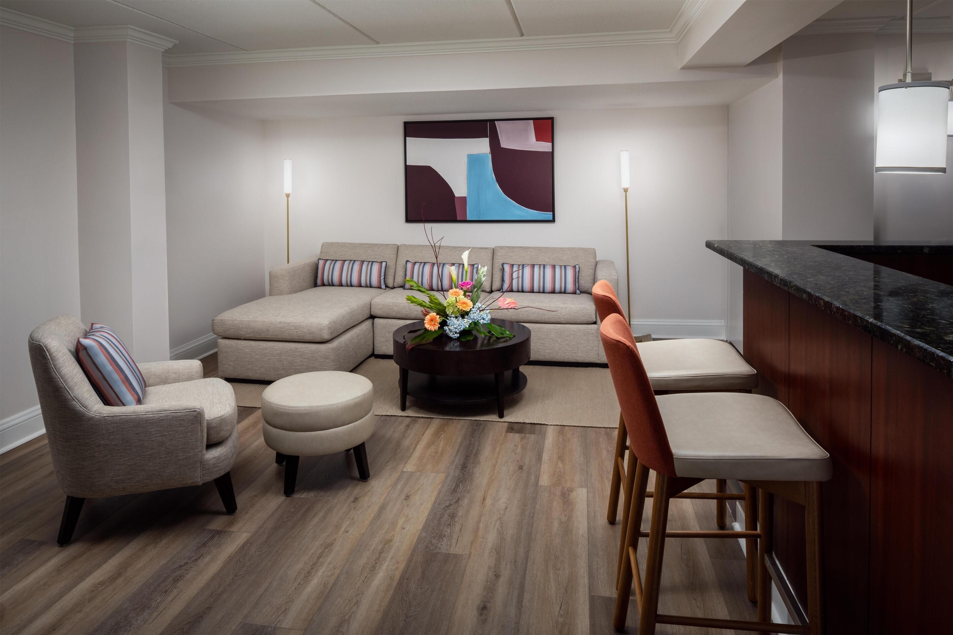 Una sala de estar moderna con un sofá seccional, dos sillones, una mesa de centro con flores y una zona de bar.