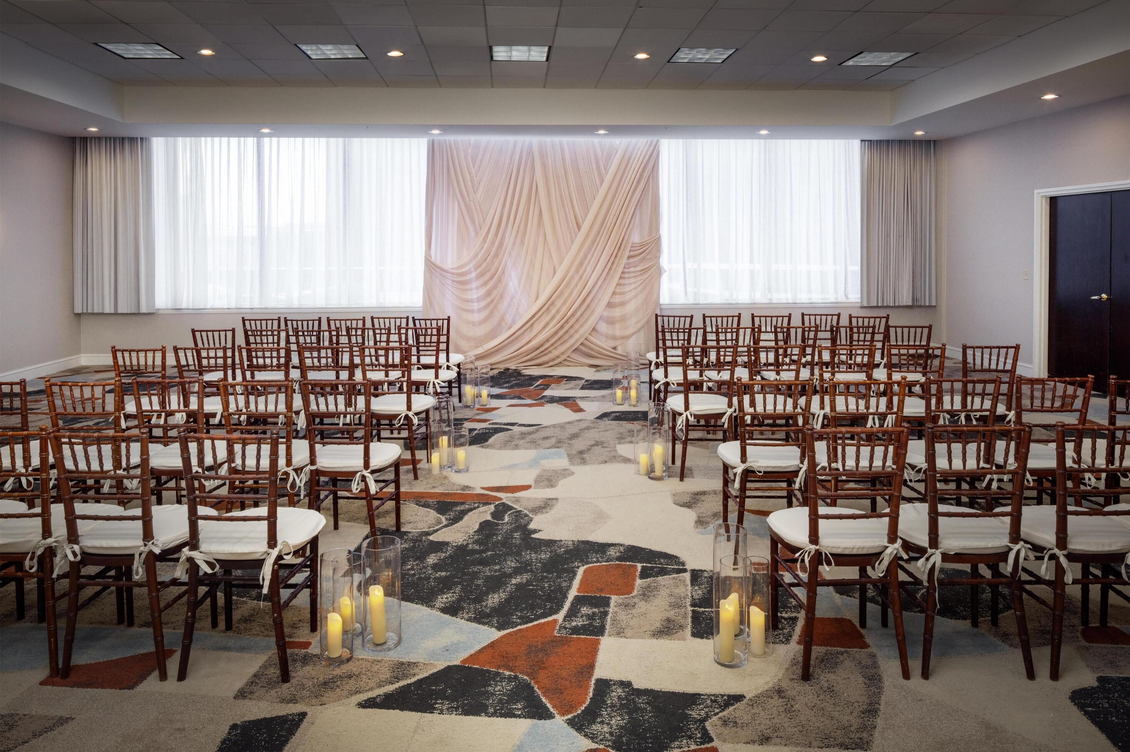A conference room with rows of wooden chairs and tables, a patterned carpet, and a large window with sheer curtains.