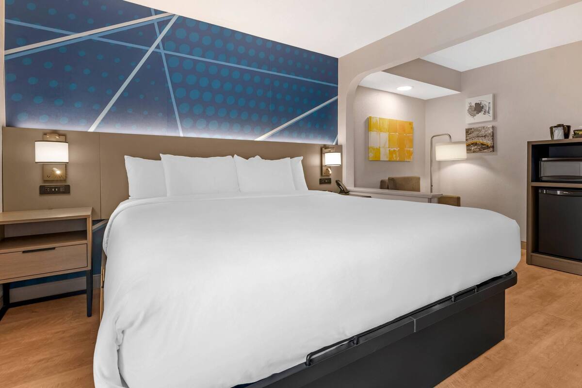 Quarto de hotel com cama grande, mesas de cabeceira, escrivaninha e design moderno na parede.