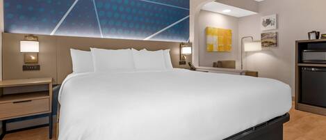 A hotel room with a large bed, bedside tables, a desk, and a modern wall design.