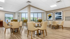 A spacious room with multiple tables and chairs, large windows, and artwork on the walls. - Comfort Inn & Suites Saint Louis Lafayette Square (St. Louis)