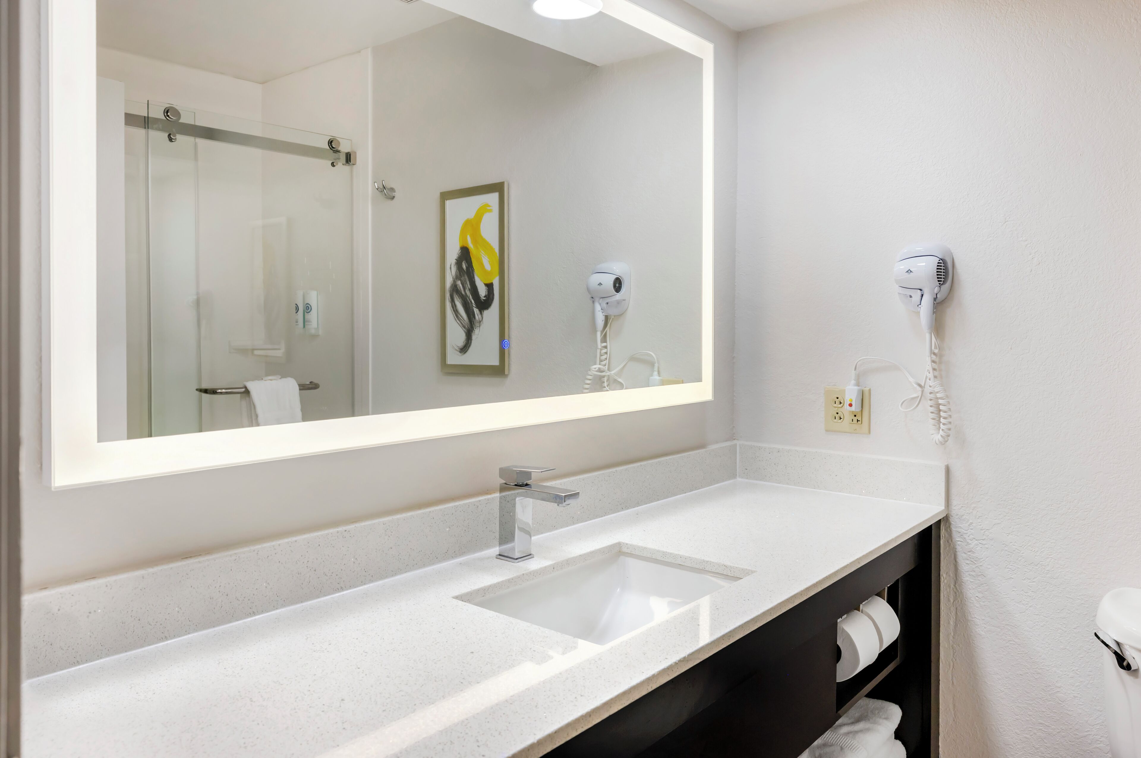 A modern bathroom with a large mirror, a sink, a hairdryer, and a telephone.