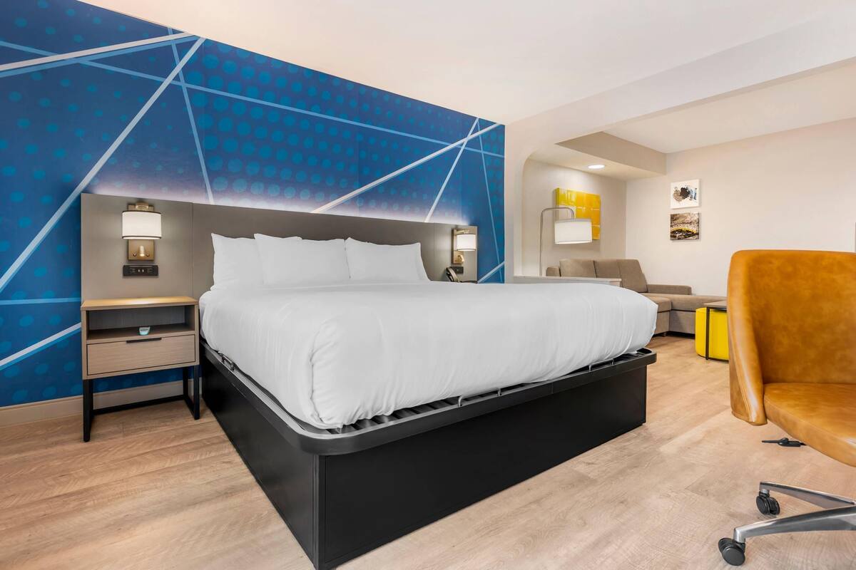 Quarto de hotel moderno com cama, mesas de cabeceira, escrivaninha e uma cadeira.