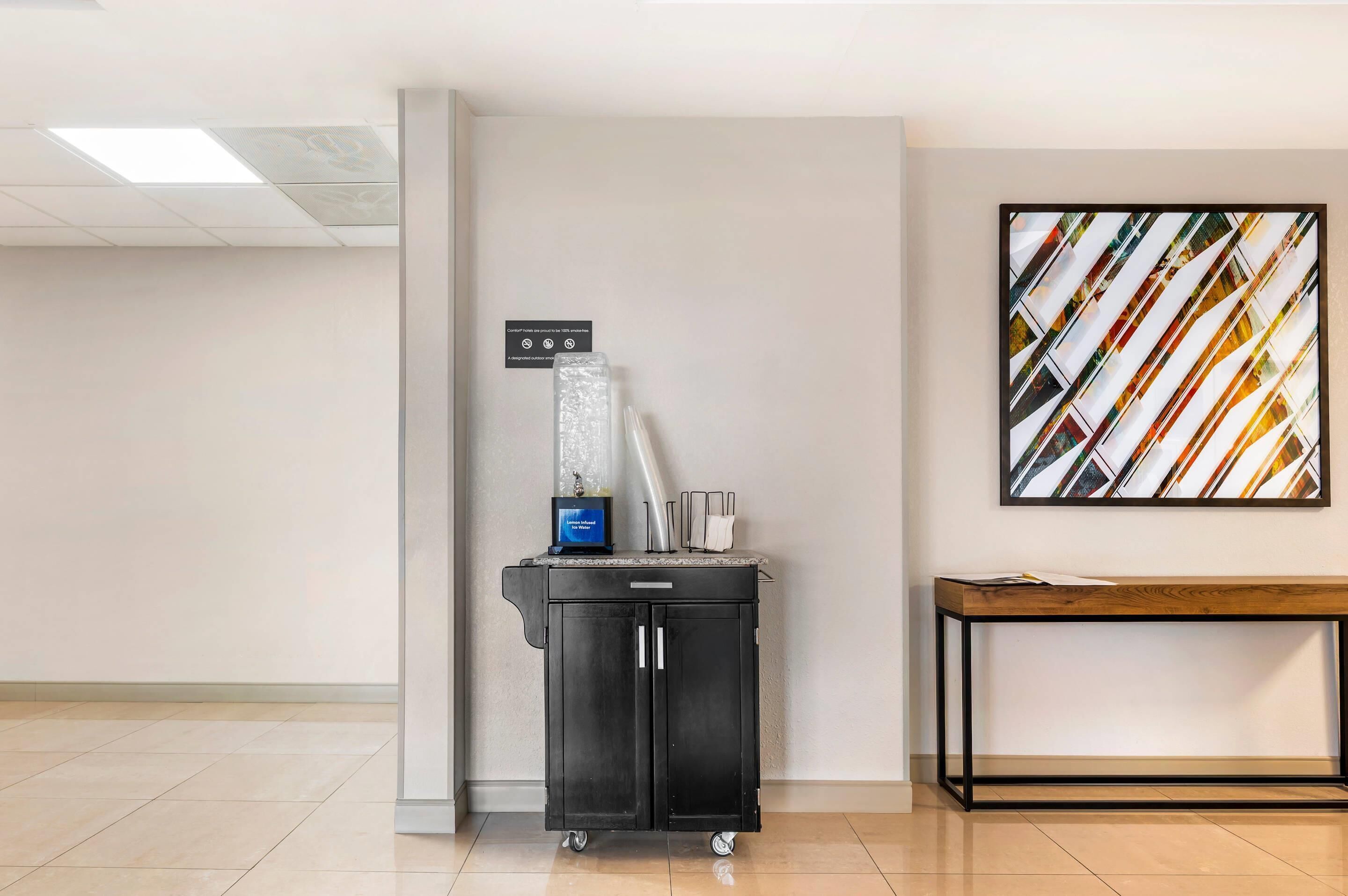 A clean, modern lobby with a water dispenser, a small table, and a wall-mounted abstract art piece.