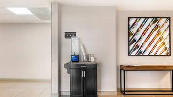A clean, modern lobby with a water dispenser, a small table, and a wall-mounted abstract art piece.
