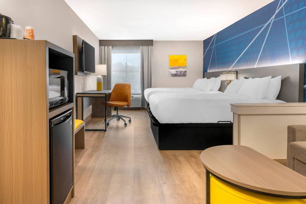 Quarto de hotel com cama, escrivaninha, cadeira e televisão.