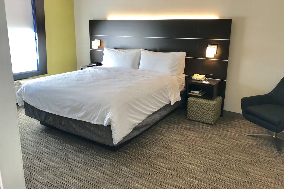 A hotel room with a large bed, a nightstand with a lamp, a chair, and a small table.
