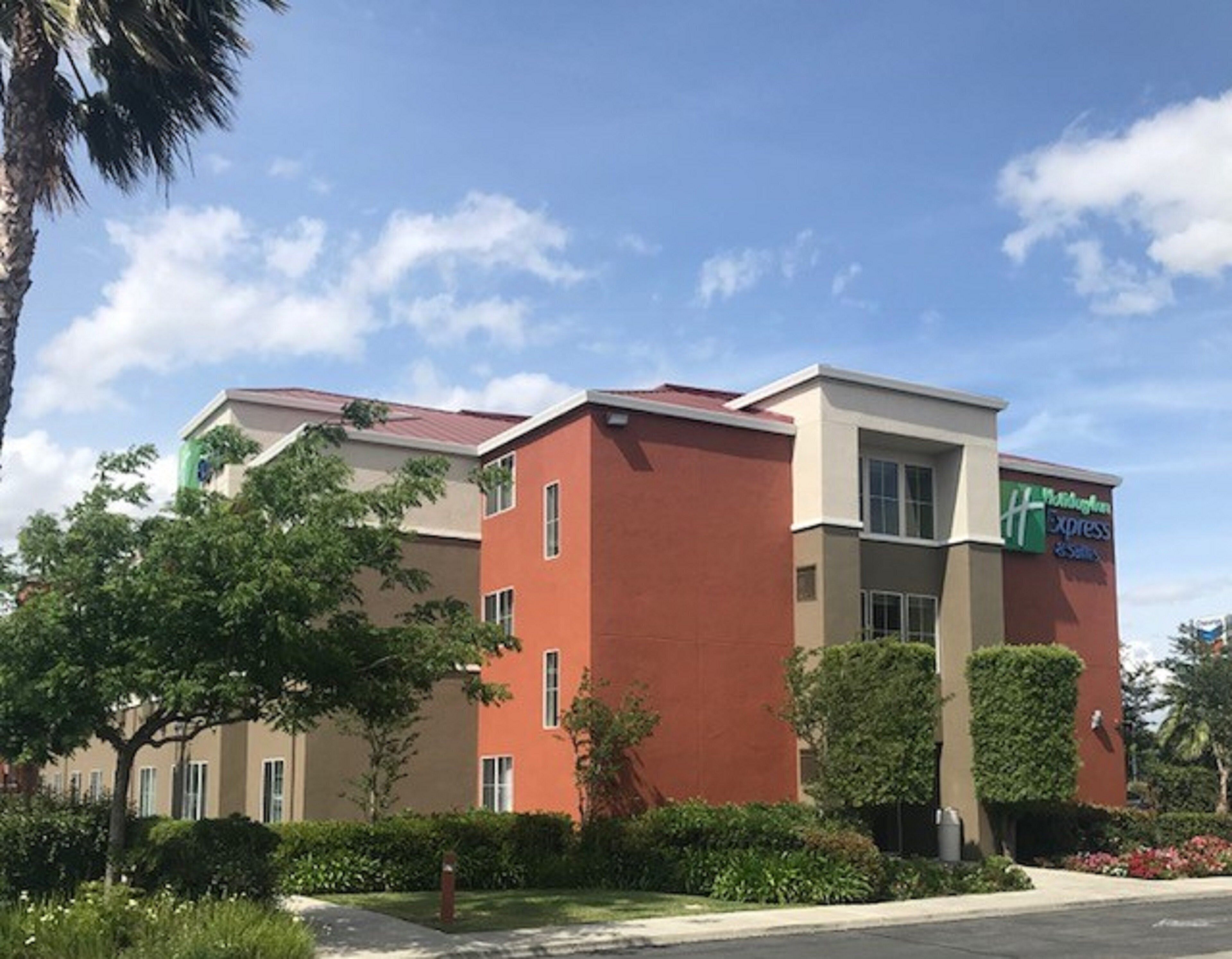 A multi-story hotel with a red facade, a visible sign for Hampton Inn Express, and a well-maintained garden area.