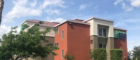 A multi-story hotel with a red facade, a visible sign for Hampton Inn Express, and a well-maintained garden area.