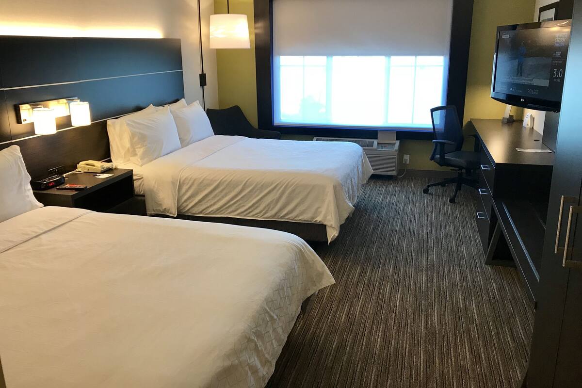 A hotel room with two beds, a desk with a computer, a TV, and a large window.