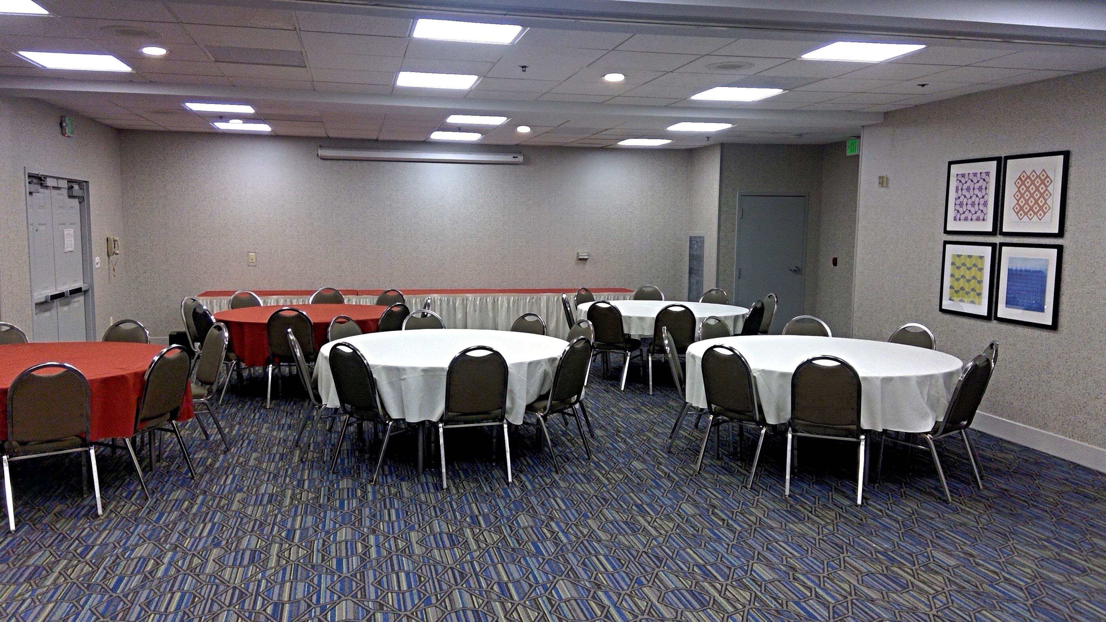 A conference room with multiple tables and chairs, carpeted floor, and ceiling lights.