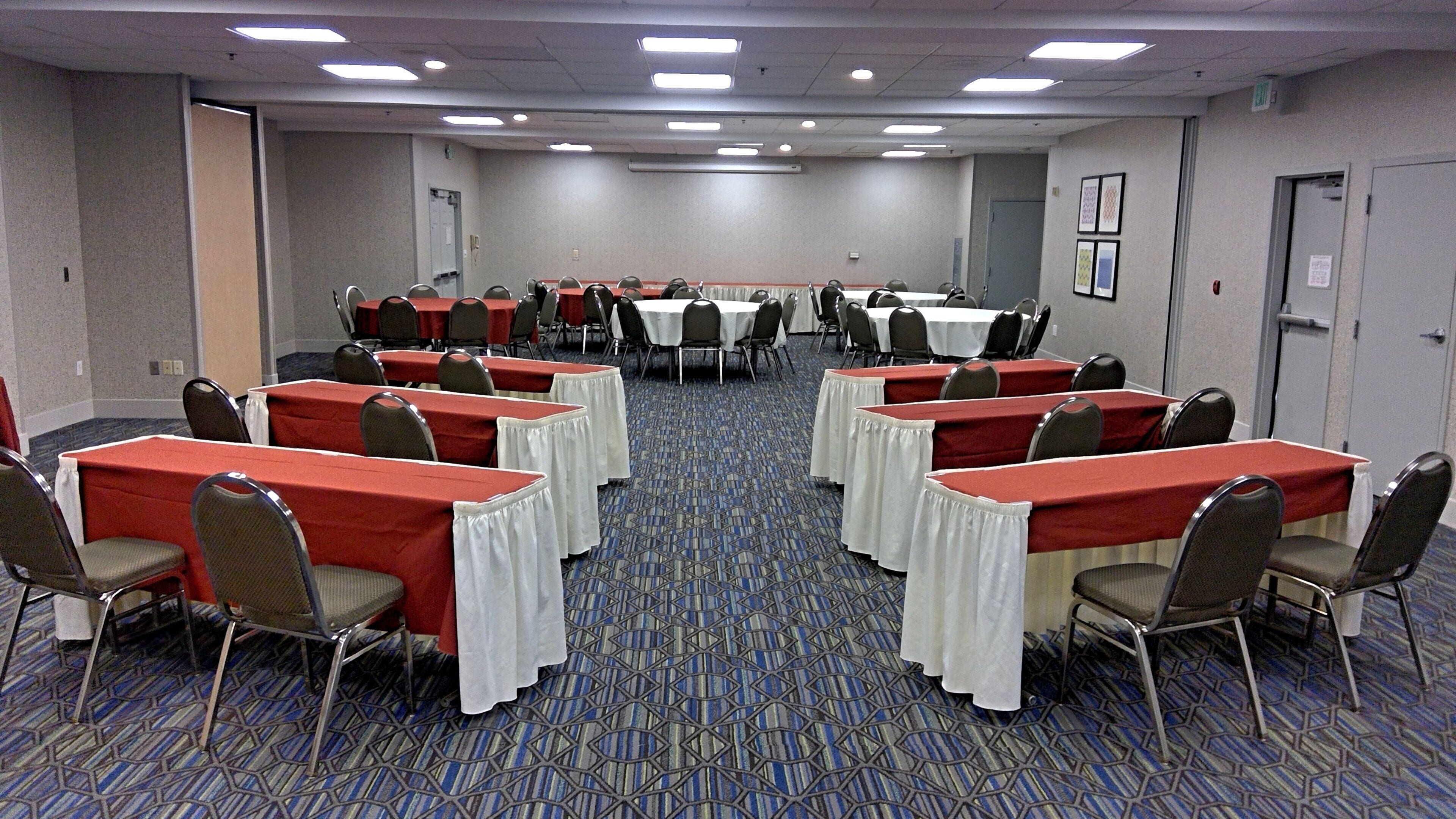 A conference room with multiple tables and chairs, carpeted floor, and ceiling lights.