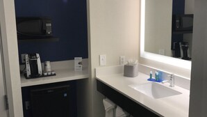 A modern bathroom with a dark blue accent wall, a large mirror, a sink, and a coffee machine.