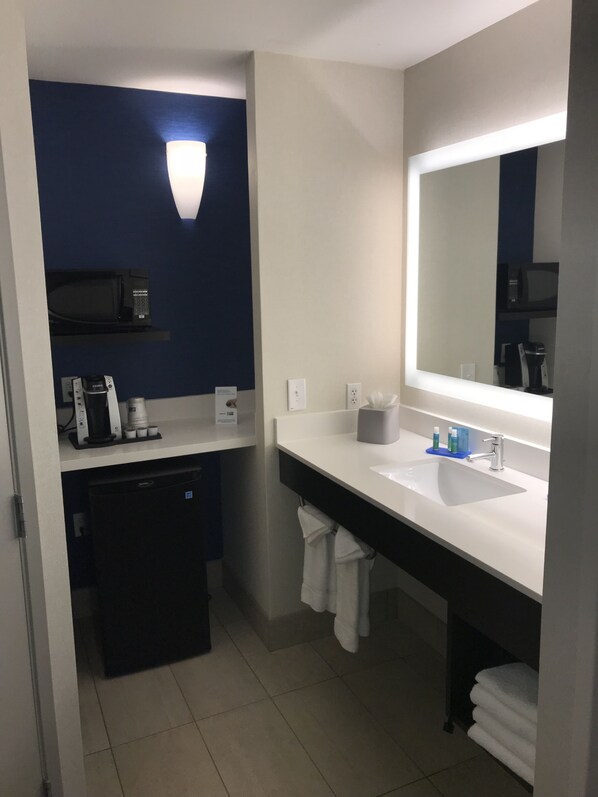 Uma casa de banho moderna com uma parede em tom azul escuro, um espelho grande, uma pia e uma máquina de café.