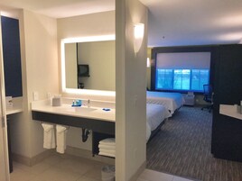 Habitación de hotel con un espejo grande, un lavamanos, una ventana con vistas y dos camas.