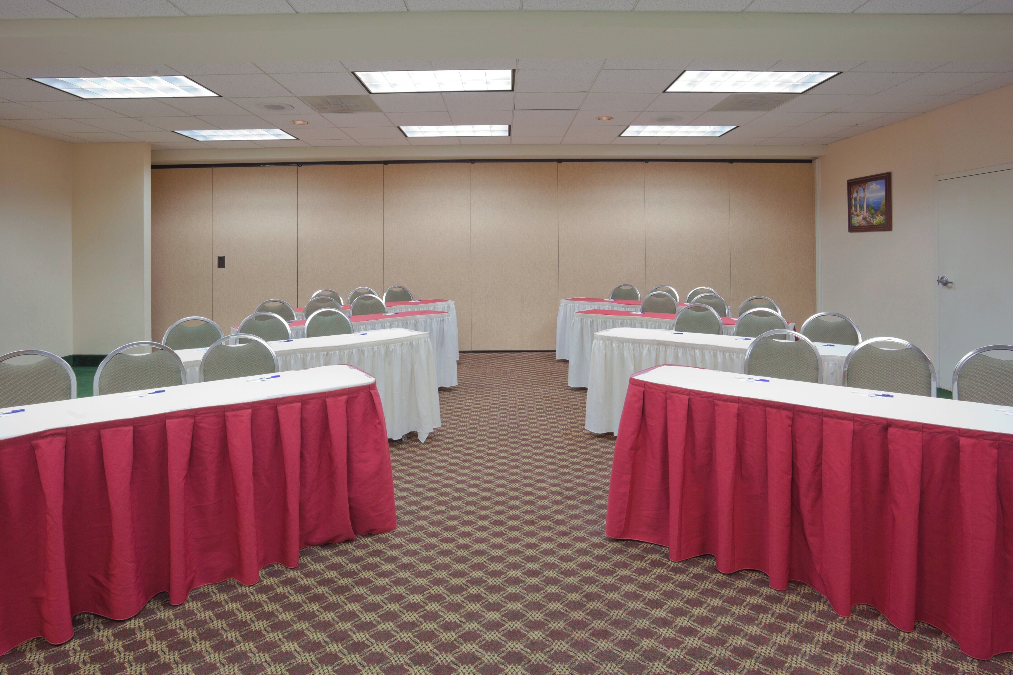 A conference room with tables and chairs, carpeted floor, and a plain wall with a door.