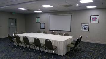 A conference room with a long table, chairs, a projector screen, and framed artwork on the walls.