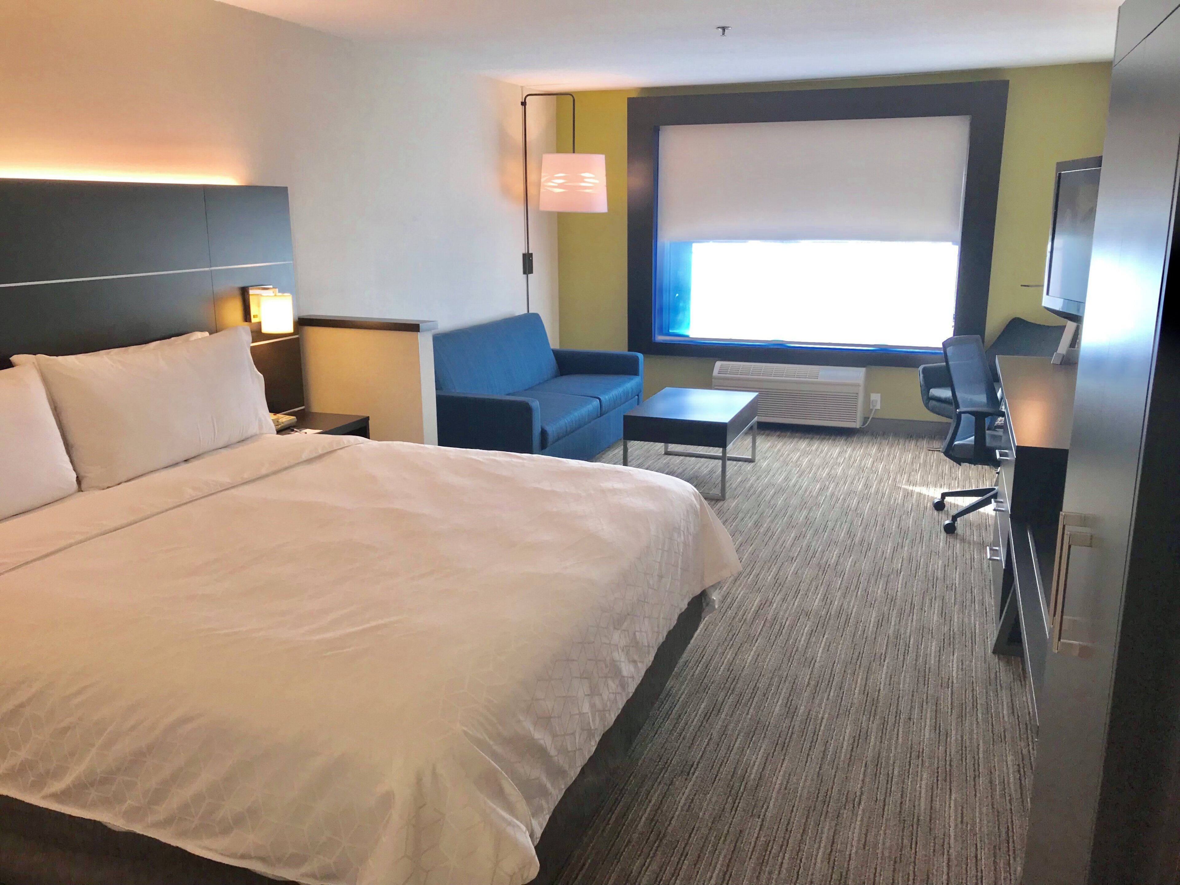 A hotel room with a large bed, a sofa, a desk, and a television.