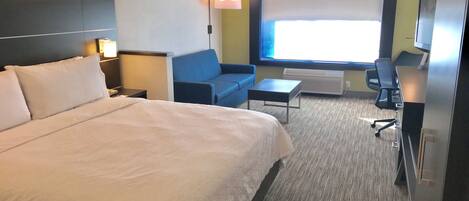 A hotel room with a large bed, a sofa, a desk, and a television.