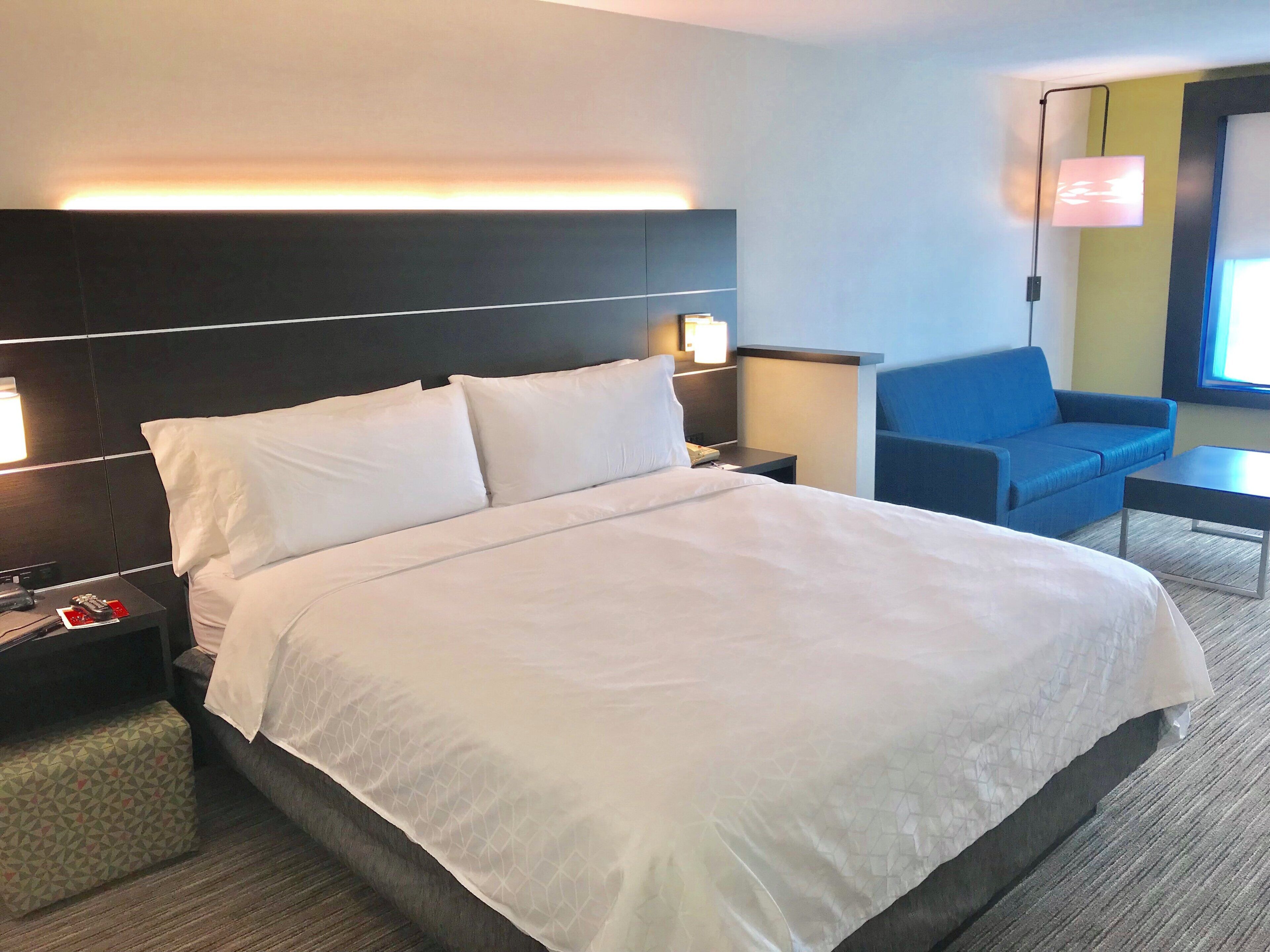 A hotel room with a large bed, bedside tables, a blue armchair, and a small table.