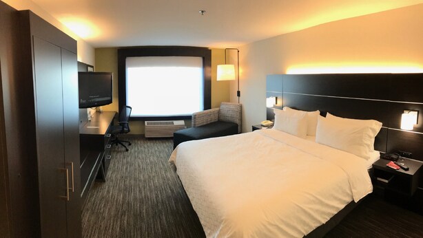A hotel room with a large bed, a desk with a computer, a television, a sofa, and a window with a view.