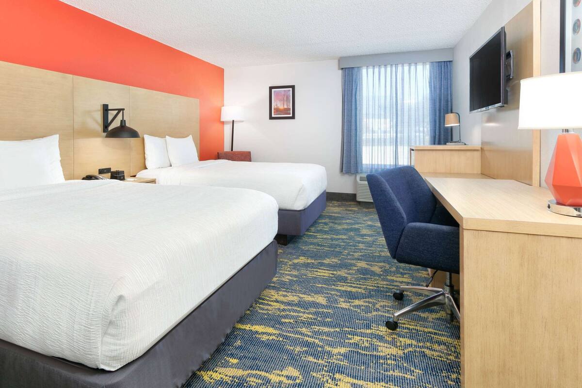A hotel room with two beds, a desk, a chair, a TV, and a window with curtains.