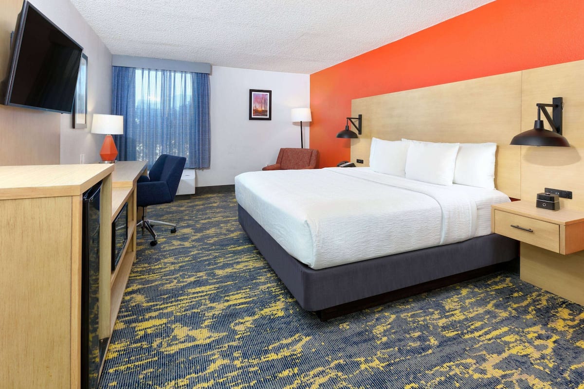 A hotel room with a bed, desk, chair, TV, and a window with curtains.