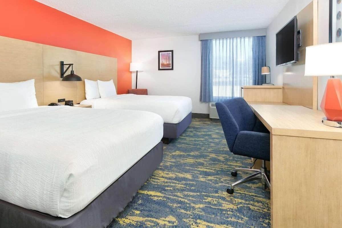 A hotel room with two beds, a desk, a chair, a TV, and a window with curtains.